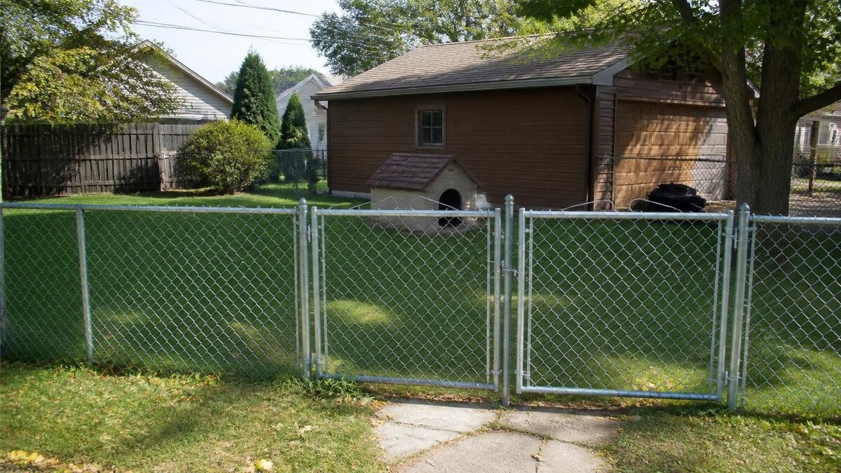 A galvanized chain link fence with a double drive gate across a backyard in front of a detached garage
