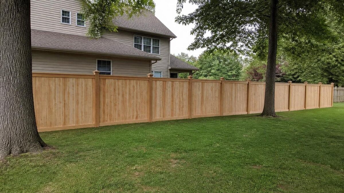 A new cedar wood privacy fence running along the back of a lawn behind a two-story house